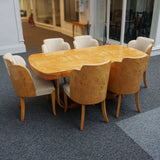 An art deco dining table with 6 chairs by Harry & Lou Epstein. The table top and cloud back armchairs are veneered in burr walnut. The chairs are upholstered in cream faux suede. 