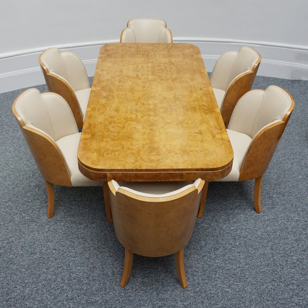 An Art Deco dining table with six chairs by Harry & Lou Epstein. The table top is burr walnut veneered. The six matching cloud backed armchairs are upholstered in cream leather