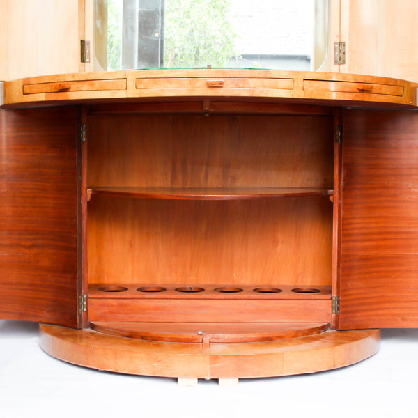 An Art Deco, demi-lune cocktail cabinet attributed to Harry & Lou Epstein. Mirrored, lit interior to top with glass shelves and mirrored slide tray. Lower, shelved cabinet with bottle holders. Burr walnut veneer at Jeroen Markies.