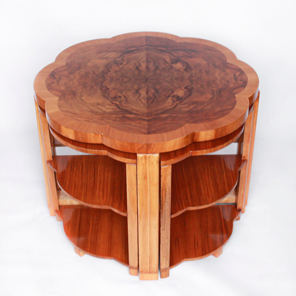 An Art Deco nest of tables in figured and straight grain walnut veneer. Main table with shaped edging set over cross footed base. Four shelved, integral side tables.