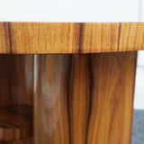 An Art Deco style centre table with a curved central column with hidden shelf to either side set over a circular base made from burr walnut veneer